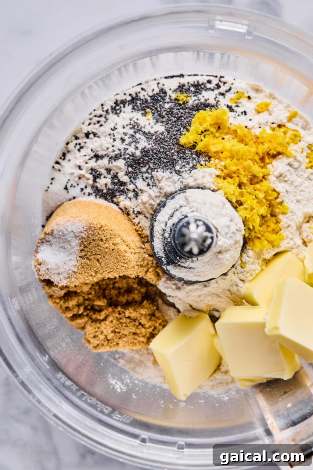 Protein-Packed Cottage Cheese Fruit Pizza 3 A food processor bowl filled with dry ingredients for the crust: flour, brown sugar, poppy seeds, and bright yellow lemon zest, along with cold cubes of unsalted butter, ready for blending.