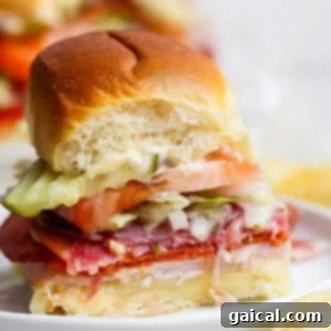 A small, mouth-watering Italian grinder slider with layers of fresh deli meats, melted cheese, crisp lettuce, juicy tomato, and pickles on a soft bun, with a bite taken out to reveal its delicious fillings. This image captures the essence of a perfect, easy-to-eat party snack.
