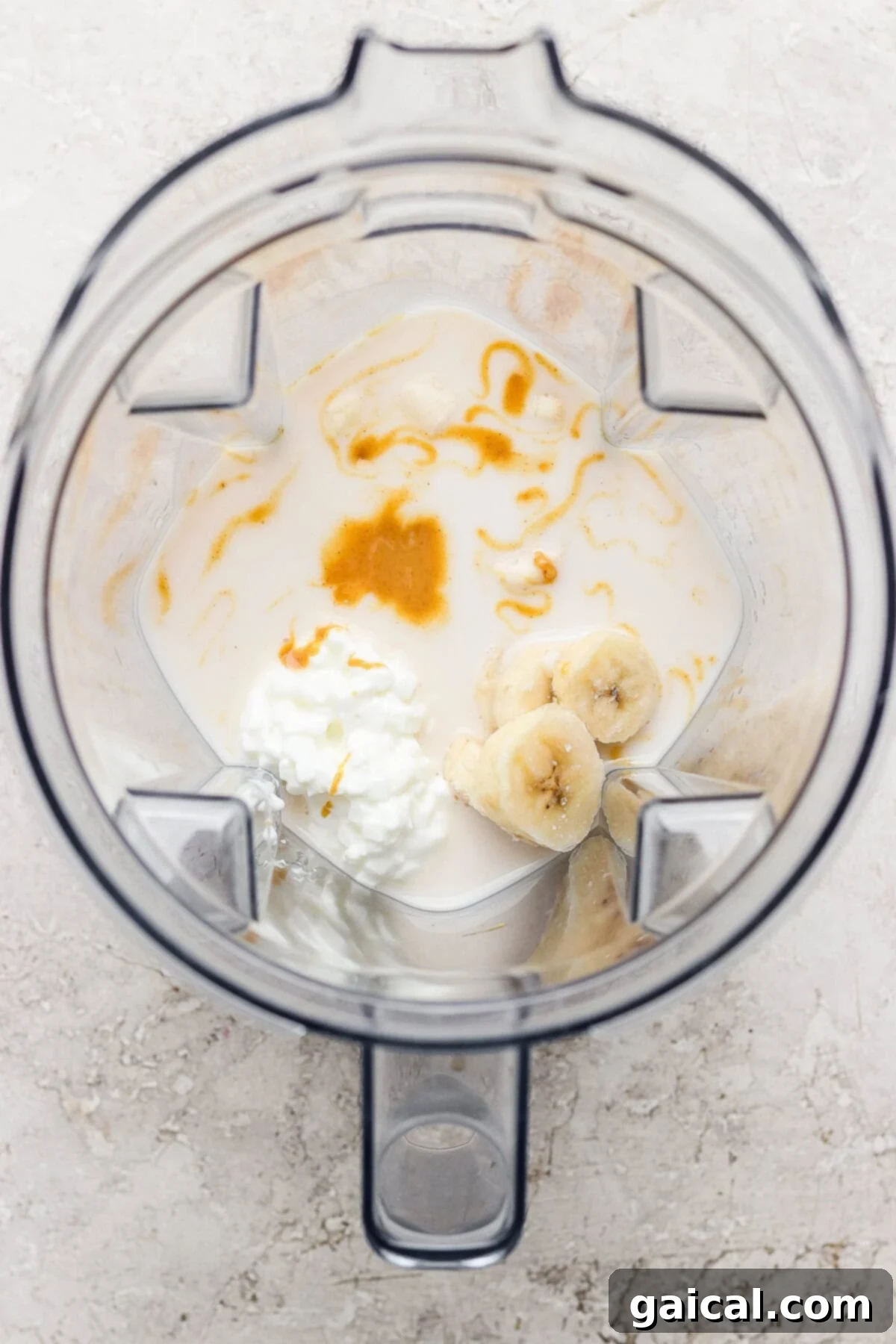 A blender containing milk, sliced banana, cottage cheese, and a drizzle of honey, viewed from above.