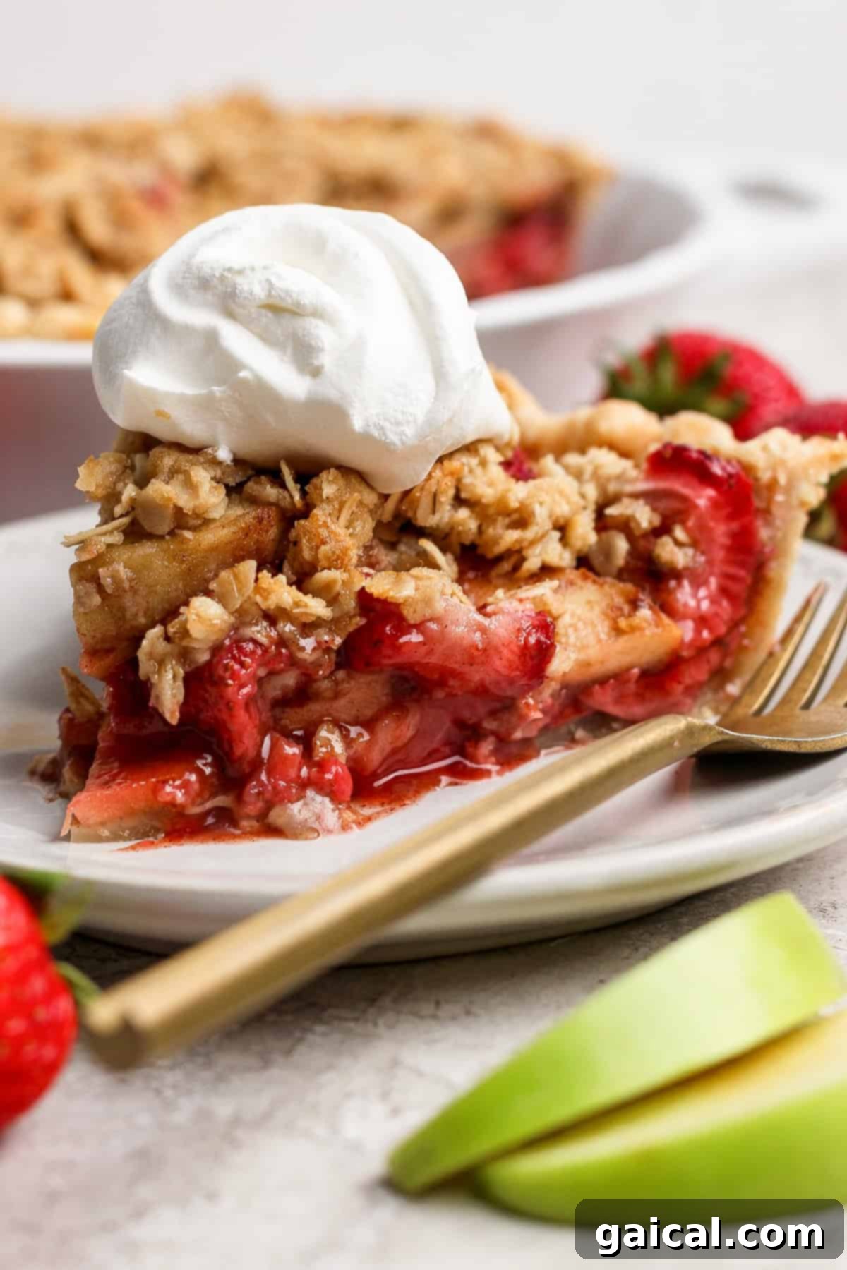 Sun-Kissed Strawberry Apple Pie 2 A perfectly sliced strawberry apple pie crumble, generously topped with fluffy whipped cream, resting on a pristine white plate. A golden fork, alongside fresh strawberries and thin apple slices, completes this enticing dessert presentation.