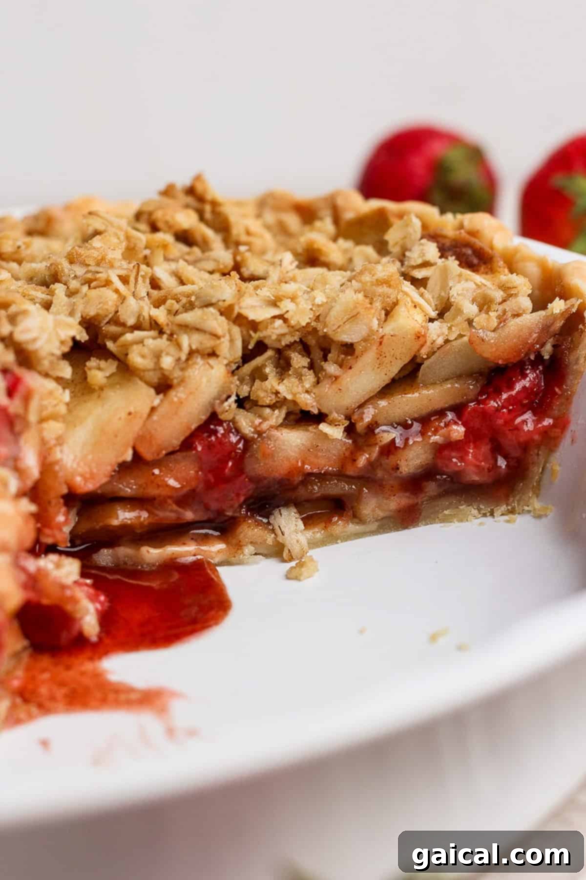 Sun-Kissed Strawberry Apple Pie 4 A tantalizing close-up of a generously sliced strawberry apple pie crumble. The golden oat topping is beautifully visible, encasing abundant layers of perfectly cooked apples and sweet strawberries within a pristine white pie dish. The filling glistens, promising rich flavor.