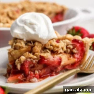A beautiful slice of strawberry apple pie crumble topped with whipped cream, served on a white plate with fresh berries in the background.
