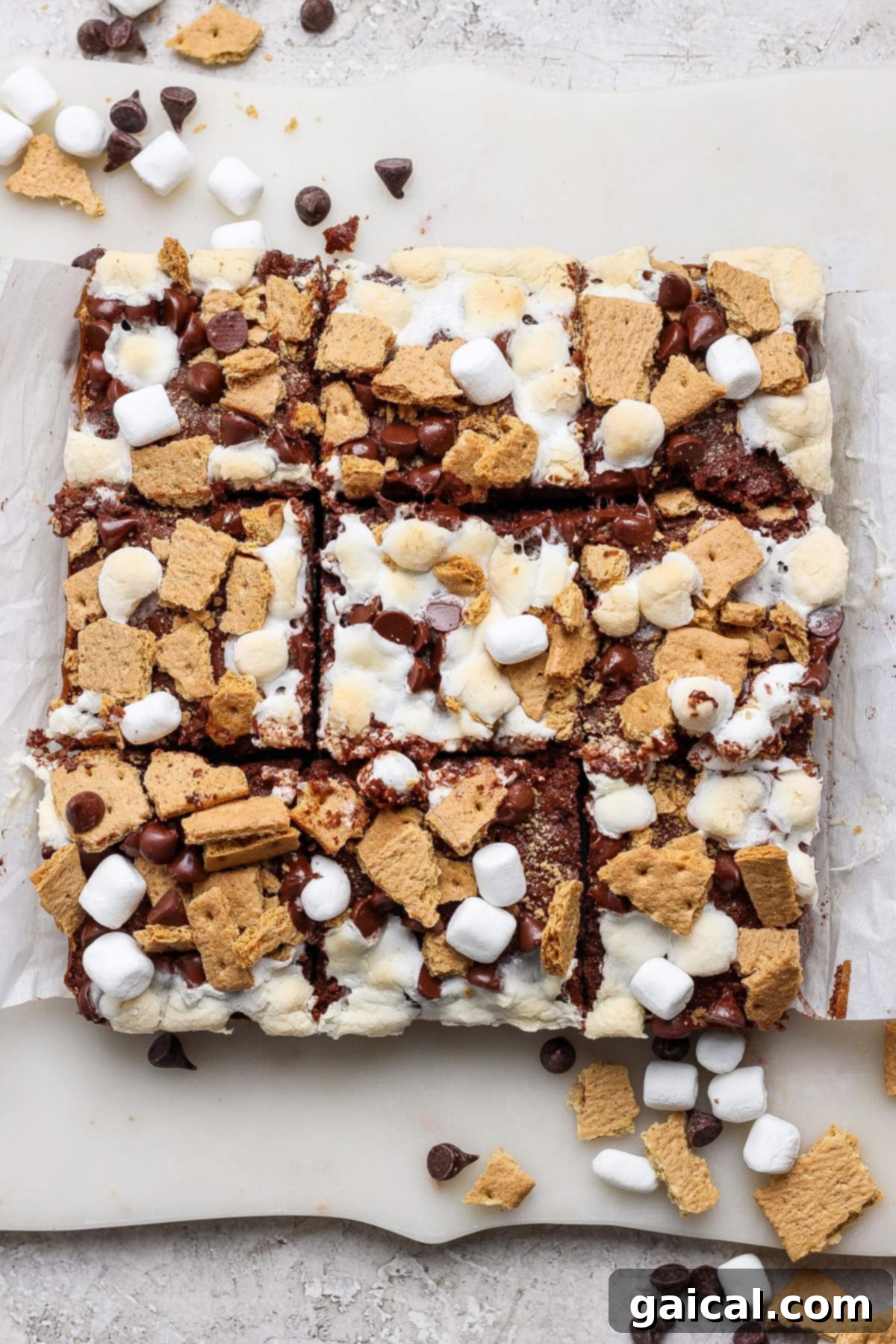 A batch of s'mores bars cut into squares, topped with mini marshmallows, graham cracker pieces, and chocolate chips on parchment paper—these treats are perfect for fans of classic s’mores brownies.