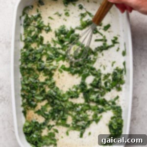 Vibrant Grilled Gnocchi Kebabs 11 A hand uses a whisk to mix chopped greens and liquid with seasonings in a white rectangular baking dish.