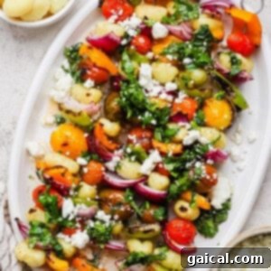 Vibrant Grilled Gnocchi Kebabs 12 A white platter with vegetable and gnocchi skewers, topped with chopped herbs and crumbled cheese, is pictured next to small bowls of cooked gnocchi and crumbled cheese.
