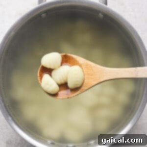 Vibrant Grilled Gnocchi Kebabs 6 A wooden spoon holds several pieces of gnocchi over a pot of boiling water.