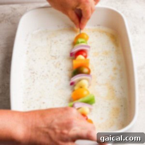 Vibrant Grilled Gnocchi Kebabs 9 A person places a skewer with vegetables—tomatoes, onions, peppers—into a white baking dish.