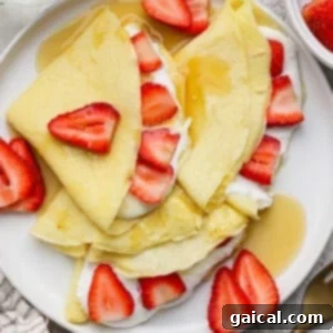 Delicious blended cottage cheese crepes, folded neatly and adorned with fresh sliced strawberries, a dollop of cream, and a drizzle of maple syrup, presented on a pristine white plate.
