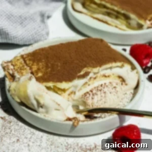 A plate of cottage cheese tiramisu crepe roll with a spoonful taken out, topped with cocoa powder, sits next to fresh raspberries on a white surface.