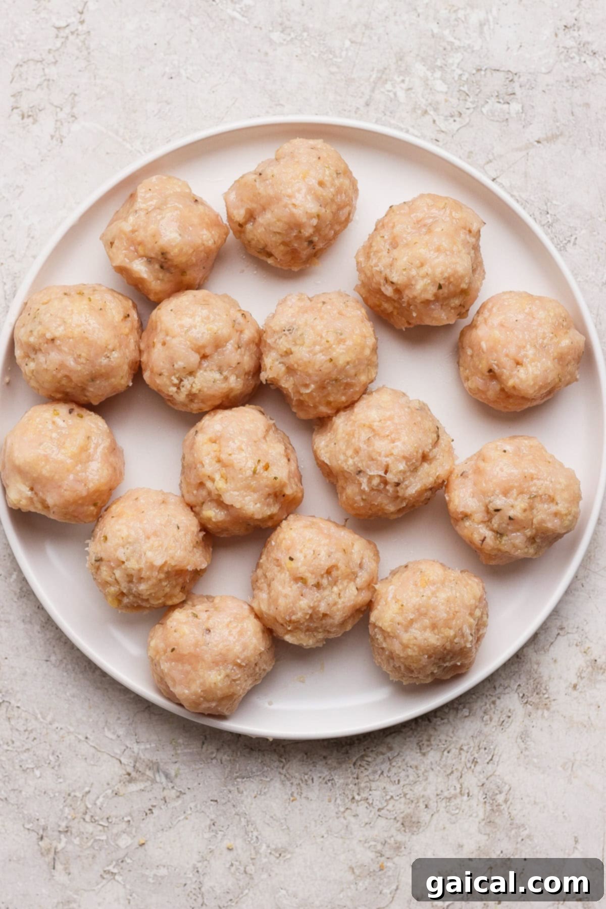 Easy Summer Skillet Orzo with Zucchini and Chicken Meatballs 4 A white plate with sixteen raw, uncooked meatballs arranged in a circular pattern on a light textured surface.