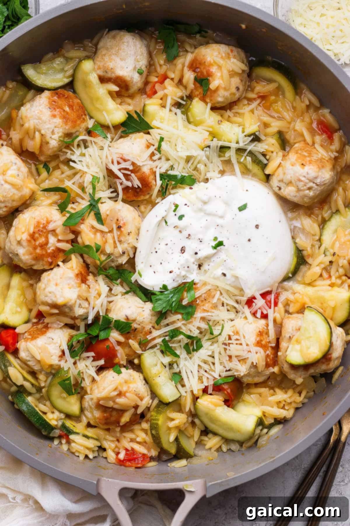 Easy Summer Skillet Orzo with Zucchini and Chicken Meatballs 7 A skillet filled with orzo pasta, chicken meatballs, sliced zucchini, red peppers, grated cheese, fresh parsley, and a dollop of burrata cheese in the center.