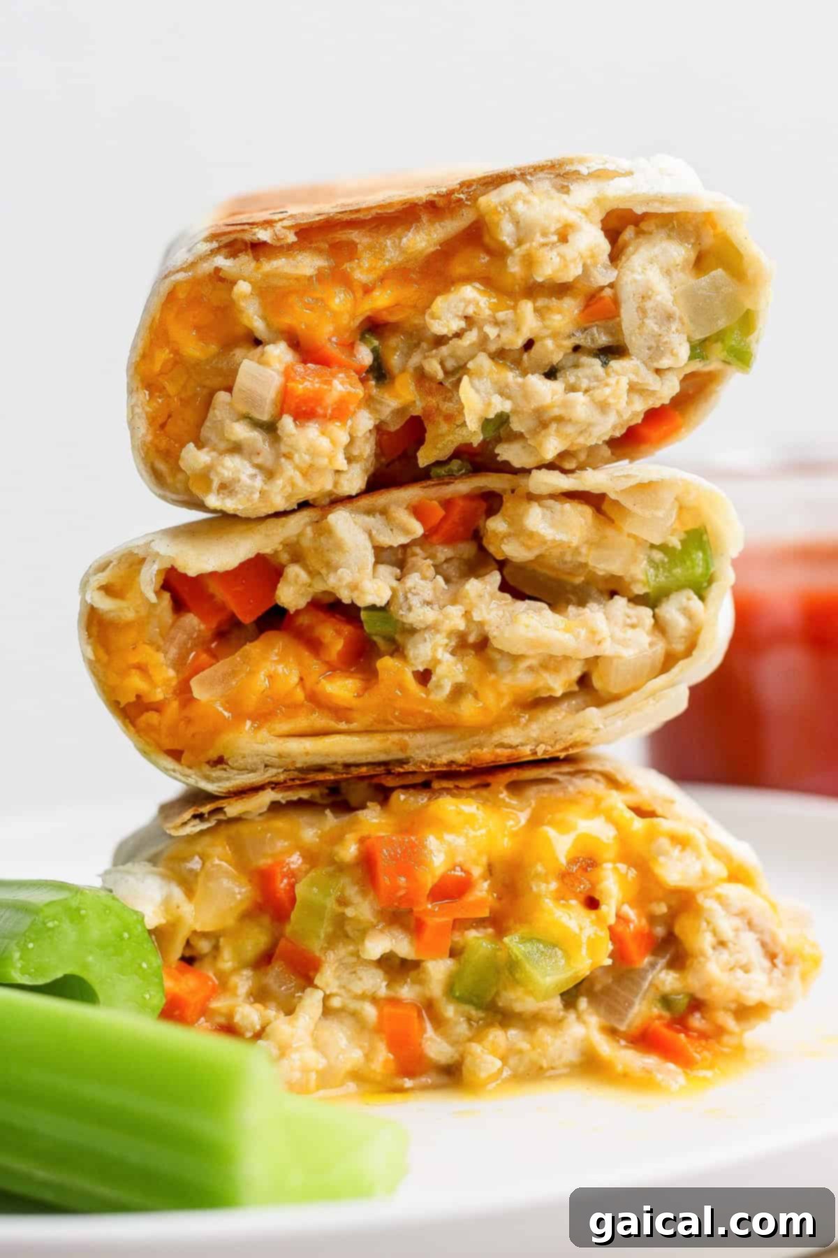 Protein Packed Buffalo Chicken Burritos 2 Three halves of a high-protein buffalo chicken burrito filled with creamy chicken mixture, served on a plate next to fresh celery sticks, highlighting the vibrant colors and appealing texture of the filling.