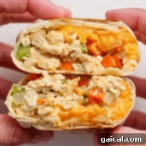 Two hands hold a halved breakfast burrito filled with scrambled eggs, cheese, onions, green peppers, and orange bell peppers.