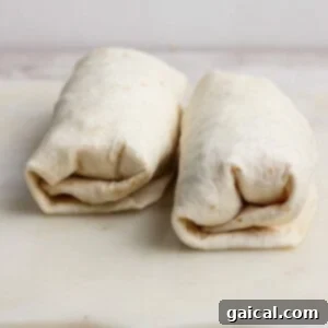 Two neatly wrapped burritos placed side by side on a white cutting board, ready for toasting or serving.