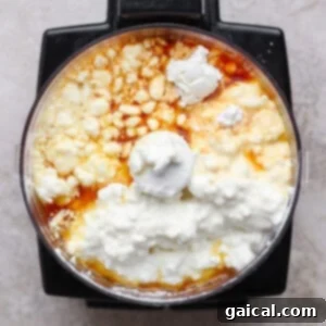 A food processor bowl filled with cottage cheese, eggs, flour, and vanilla extract, viewed from above.
