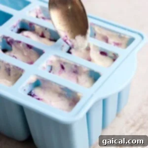 A spoon fills a blue silicone mold tray with a white and purple mixture on a light-colored surface.