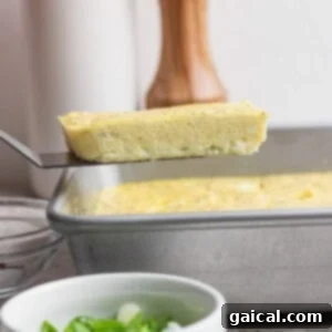A spatula lifts a rectangular slice of baked egg from a metal pan; a bowl of chopped green onions sits in the foreground.