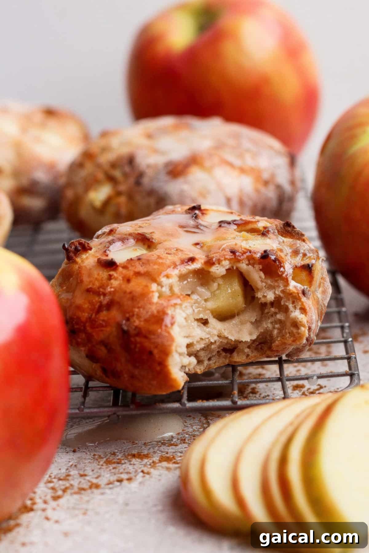 Golden Air Fried Apple Fritters with Sweet Glaze 2 A partially eaten apple fritter with glaze, sitting on a cooling rack, surrounded by whole apples and fresh apple slices, evoking a cozy fall atmosphere.