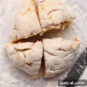 A round ball of uncooked dough cut into four equal pieces on floured parchment paper, with a knife placed beside it, ready for shaping.