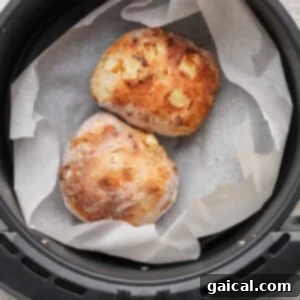 Two small, golden-brown apple fritters with a rustic crust rest on parchment paper inside an air fryer basket after cooking.