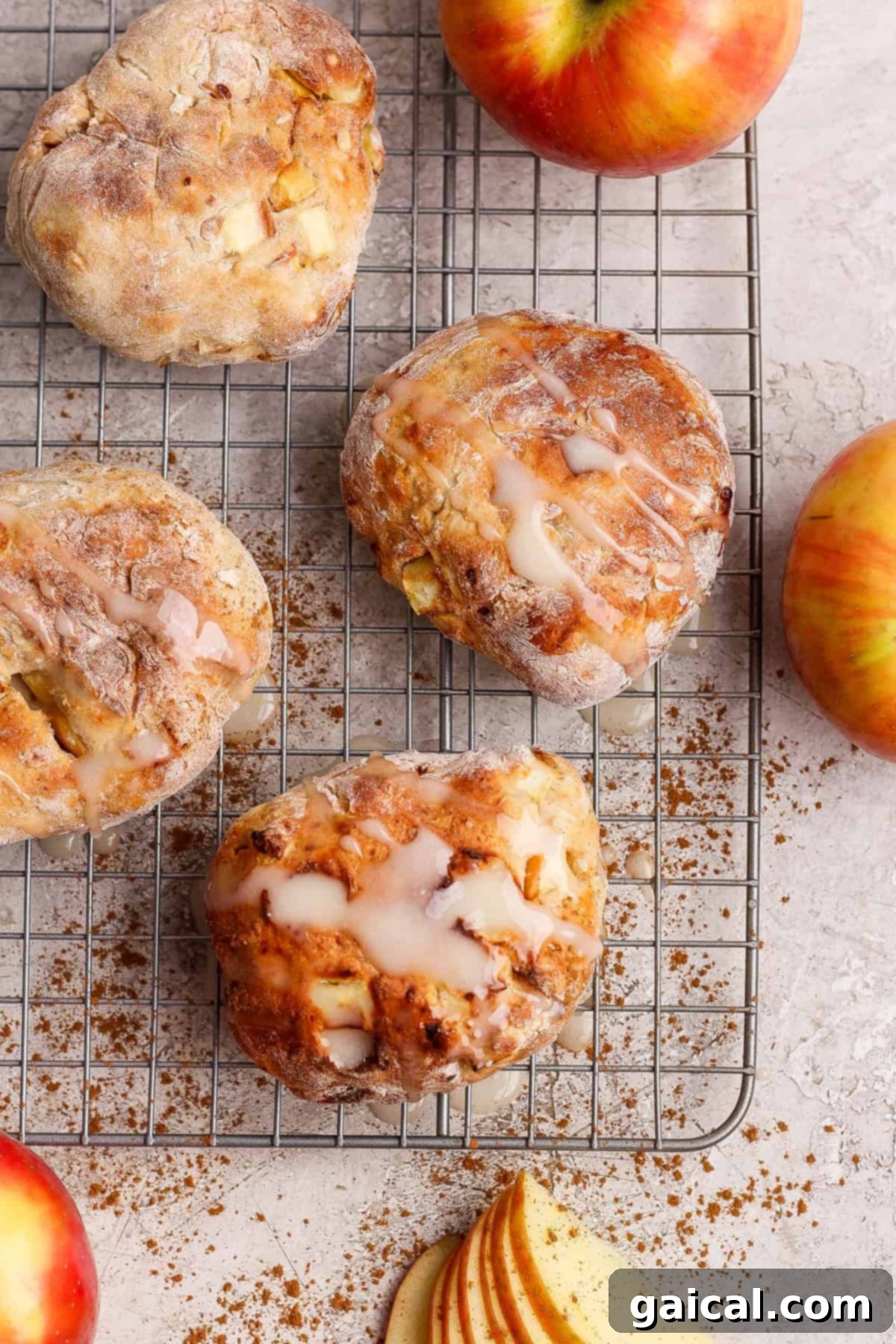 Golden Air Fried Apple Fritters with Sweet Glaze 4 Four perfectly glazed apple fritters arranged on a cooling rack, surrounded by fresh apples, whole cinnamon sticks, and decorative apple slices, all set on a light, inviting surface.