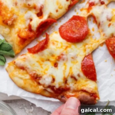 A hand holds a delicious slice of pepperoni pizza, showcasing a perfectly bubbly, melted cheese topping and a golden, crispy crust, all made with our special no-rise protein pizza dough.