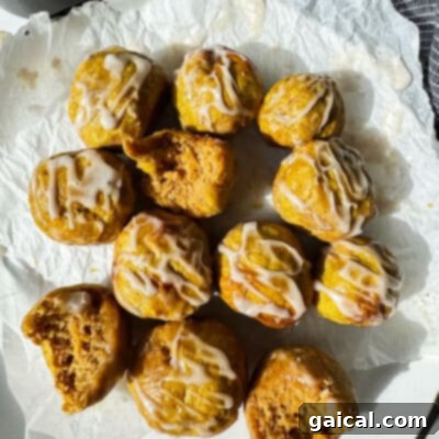 A charming dozen of small, perfectly golden-brown bagel bites, artfully drizzled with delicate white icing. Some bites reveal a tempting interior where a bite has been taken, all gracefully arranged on crumpled parchment paper under the soft, inviting glow of natural light.