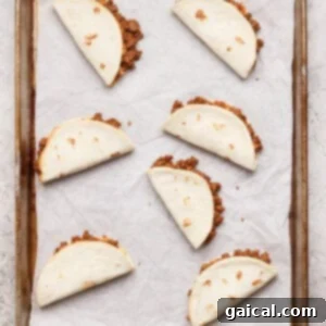 Six folded flour tortillas filled with ground beef are arranged on a parchment-lined baking sheet.