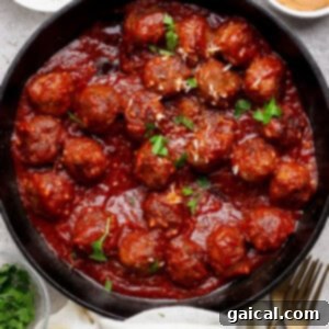 A cast iron skillet filled with savory sloppy joe meatballs covered in a rich tomato sauce, garnished with fresh parsley. Bowls of grated cheese, extra sauce, and chopped herbs surround the skillet on a rustic wooden surface, inviting you to dig in.