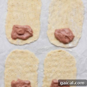 Gourmet Strawberry Toaster Tarts 12 Four rectangular dough pieces, each with fork marks and a portion of meat paste on one end, are arranged on a parchment-lined surface.