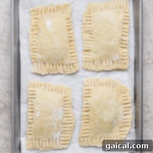 Gourmet Strawberry Toaster Tarts 13 Four unbaked rectangular hand pies with crimped edges are arranged on a parchment-lined baking sheet.