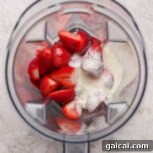 Gourmet Strawberry Toaster Tarts 8 Overhead view of a blender containing halved strawberries and a scoop of white powder on a light textured surface.