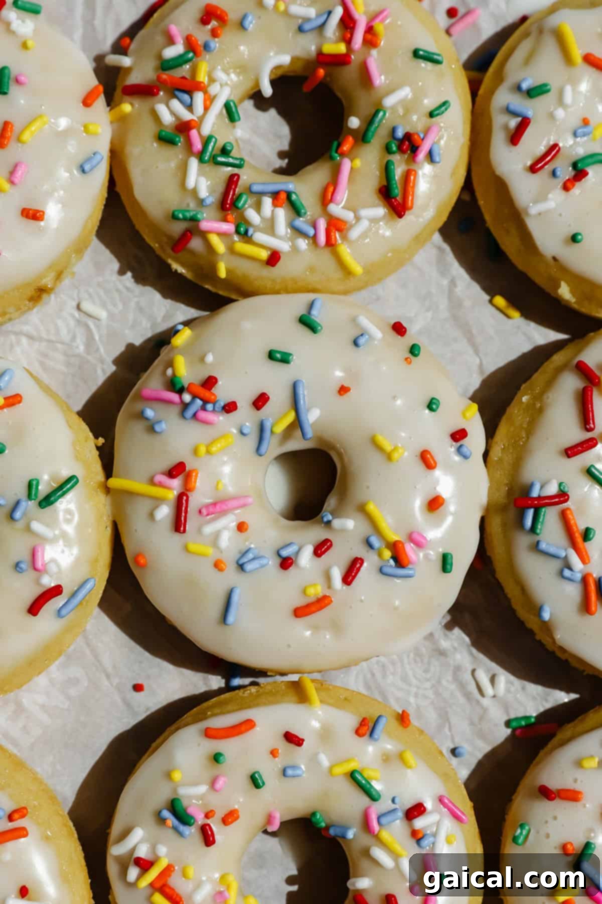 Glazed donuts topped with colorful sprinkles are arranged closely together on a light surface, showcasing their delicious appeal and fluffy texture.