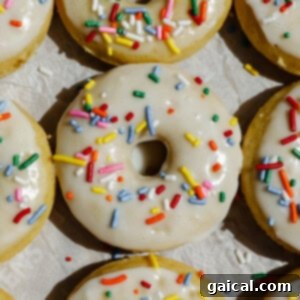 A close-up of vanilla-frosted donuts topped with colorful sprinkles arranged on parchment paper.