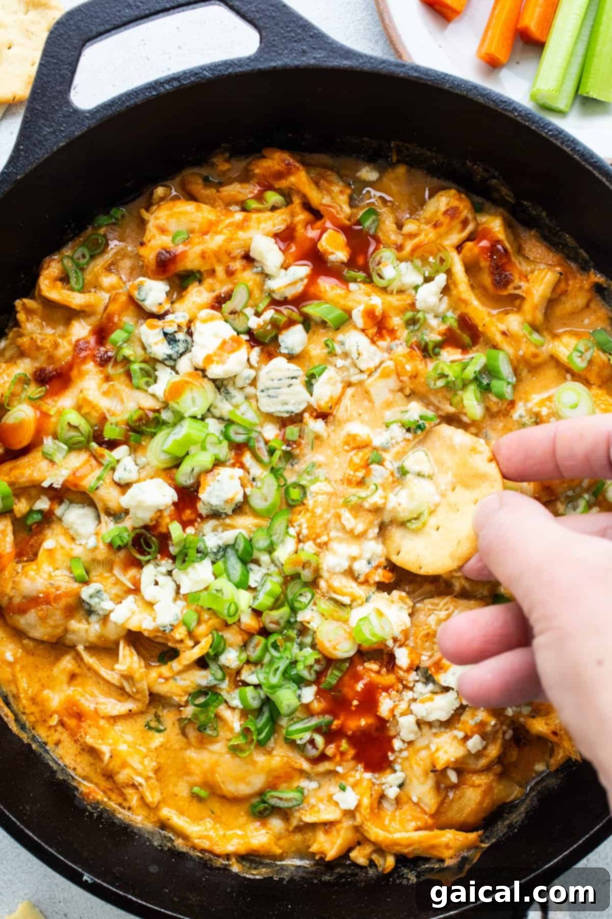 A person dipping a chip into a skillet of bubbling buffalo chicken dip, garnished with fresh herbs, hinting at a delicious fall appetizer perfect for sharing.
