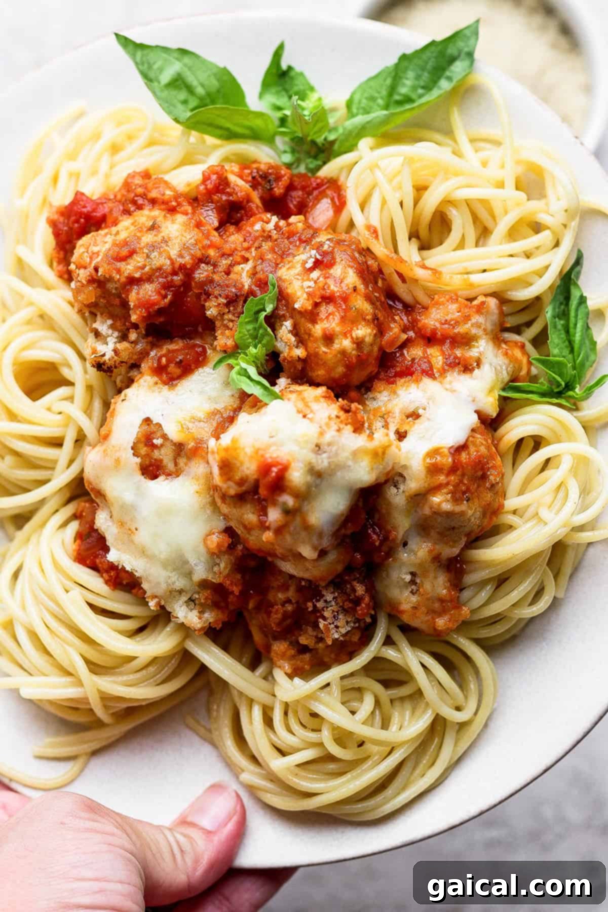 One Pan Parmesan Chicken Meatball Feast 5 A plate of spaghetti topped with meatballs, tomato sauce, melted cheese, and garnished with fresh basil leaves.