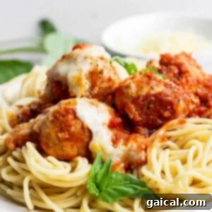 A plate of spaghetti topped with tomato sauce, meatballs, melted cheese, and a fresh basil garnish.