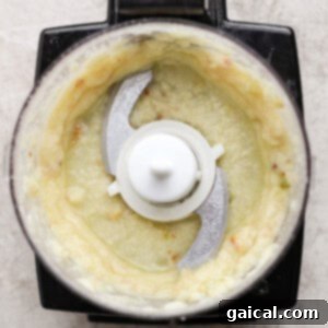 Top view of a food processor containing a pale, creamy blended mixture with visible metal blades in the center, ready to be incorporated into the salad.