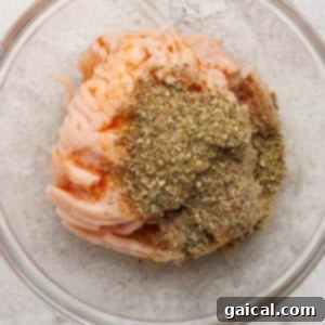 Raw ground chicken seasoned with Italian herbs in a clear bowl.