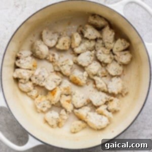 Chunks of cooked chicken scattered in a white enameled pot.