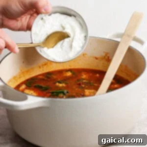 A person pouring blended cottage cheese into a pot of soup.