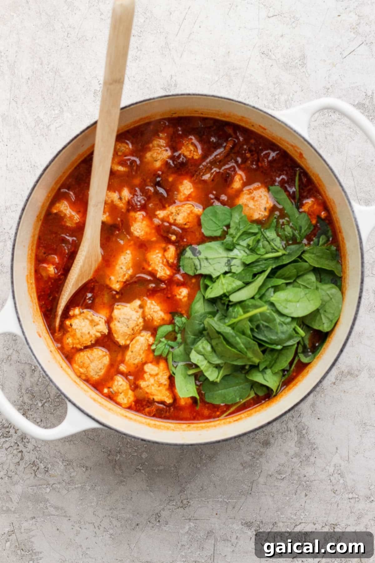 Fresh spinach wilting into the warm, savory broth of Marry Me Chicken Soup, stirred with a wooden spoon.