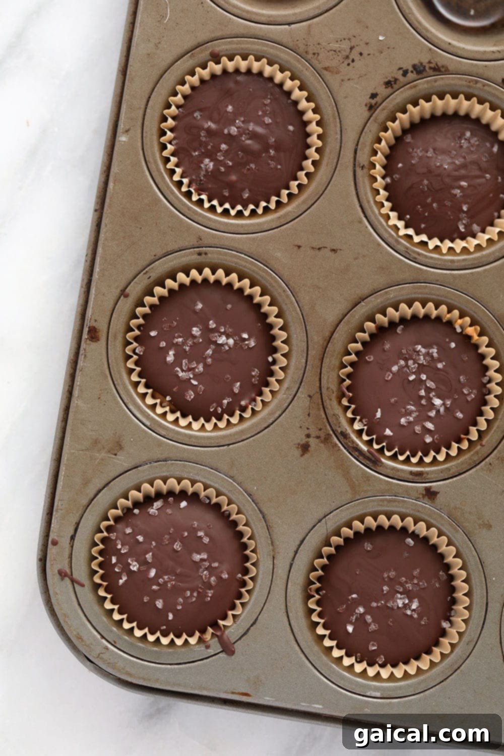 Close-up of freshly made almond butter cups in a mini muffin tin, showing the smooth chocolate and creamy almond butter layers.