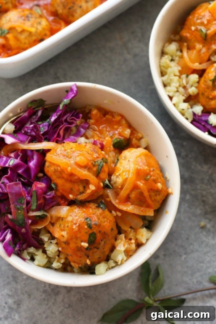 Delicious Red Coconut Curry Meatballs served in a bowl with cauliflower rice and fresh basil