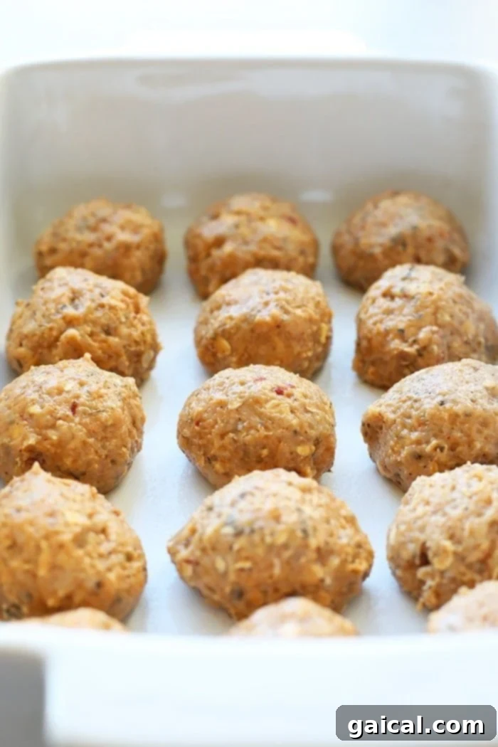 Meatballs simmering in a rich curry sauce in a baking dish, ready for oven