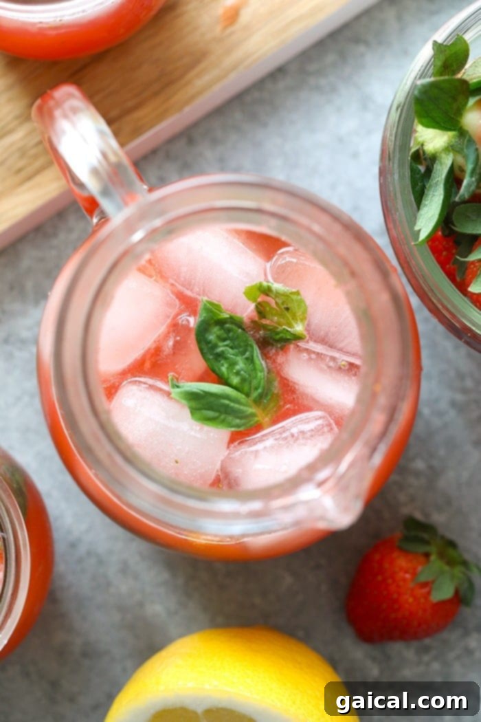 Berry Lemonade Bliss 6 A large, clear glass pitcher filled to the brim with vibrant homemade strawberry basil lemonade, artfully garnished with fresh lemon slices, whole strawberries, and fragrant basil leaves.