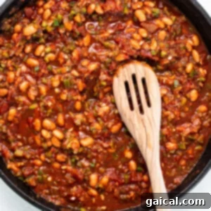 Rich tomato-based sauce simmering with beans in a cast iron pan, creating a fragrant base for the chilaquiles.