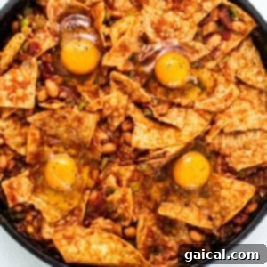Fresh eggs cracked into wells within the sauced tortilla chips, ready for baking.