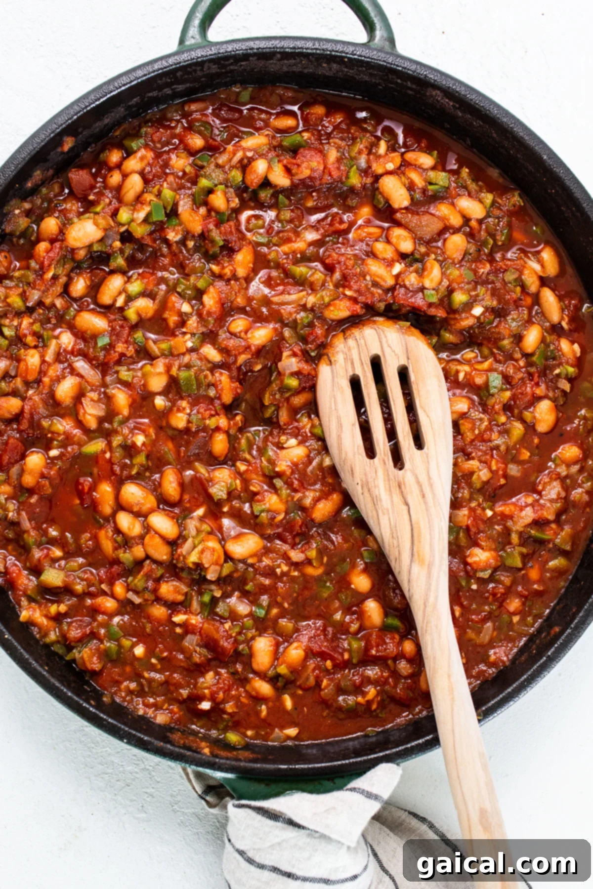 Rich tomato-based sauce simmering with flavorful pinto beans in a cast iron pan, forming the vibrant and hearty base for chilaquiles.