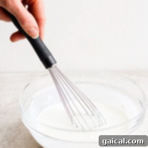 A person whisking milk in a glass bowl.
